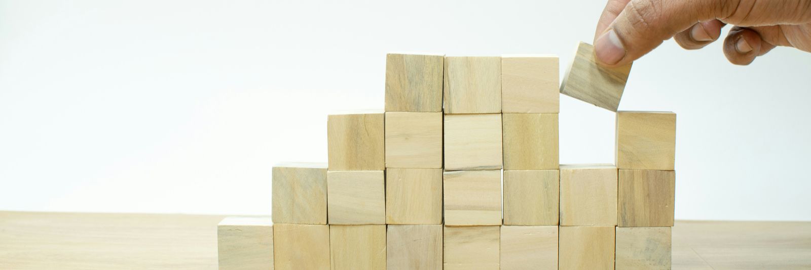 A person placing a block into a pile of wooden blocks