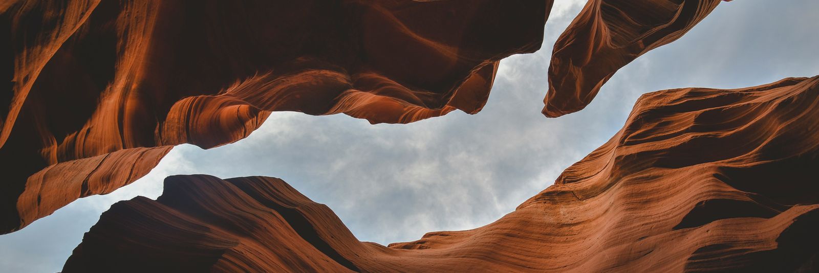 A view of the cloudy sky through the orange sandstone walls of Antelope Canyon