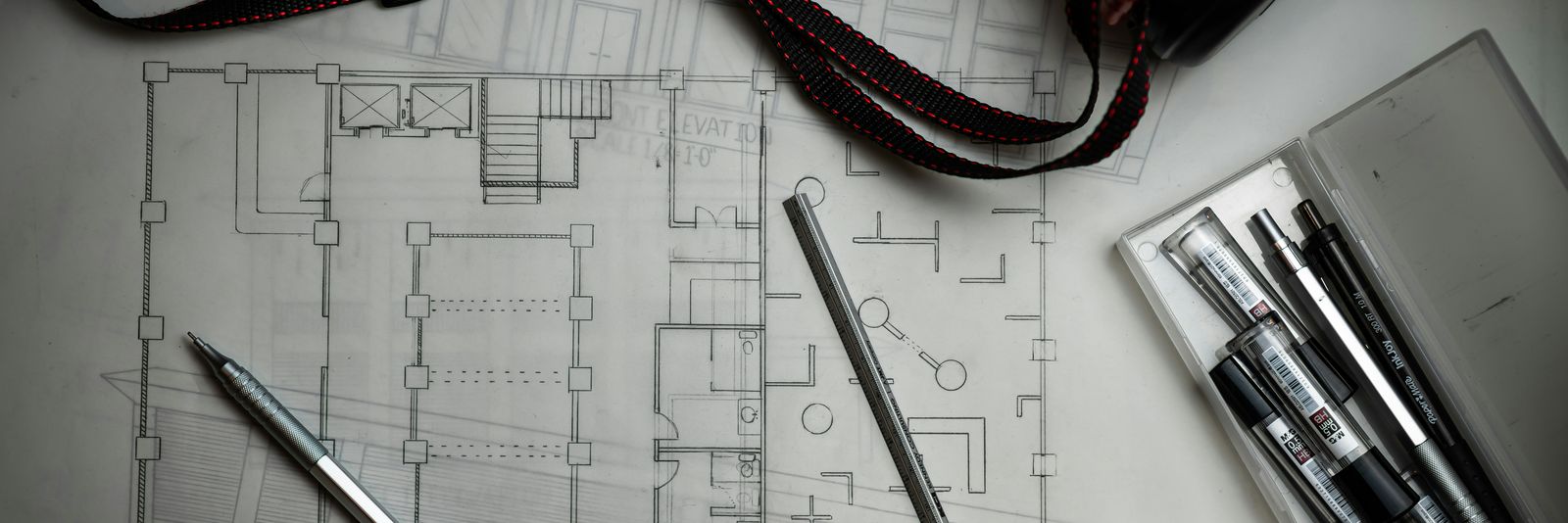 Architectural blueprints with drafting pencils, a metal ruler, and a storage tube