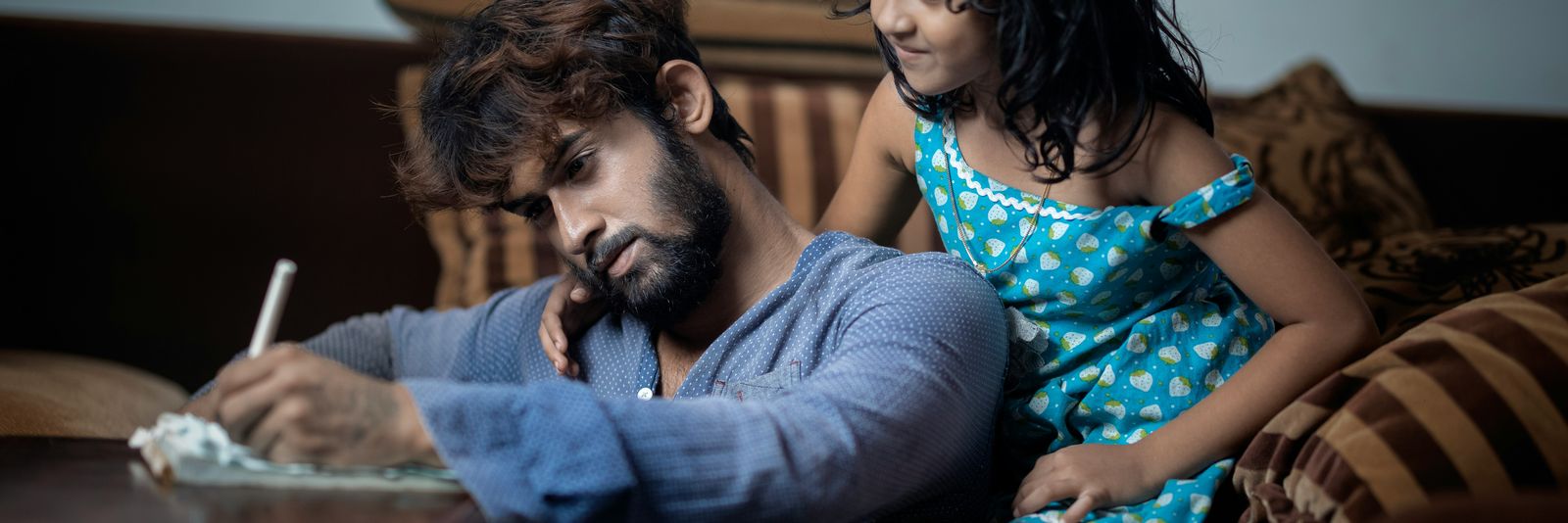 A man writes while a young girl watches him intently